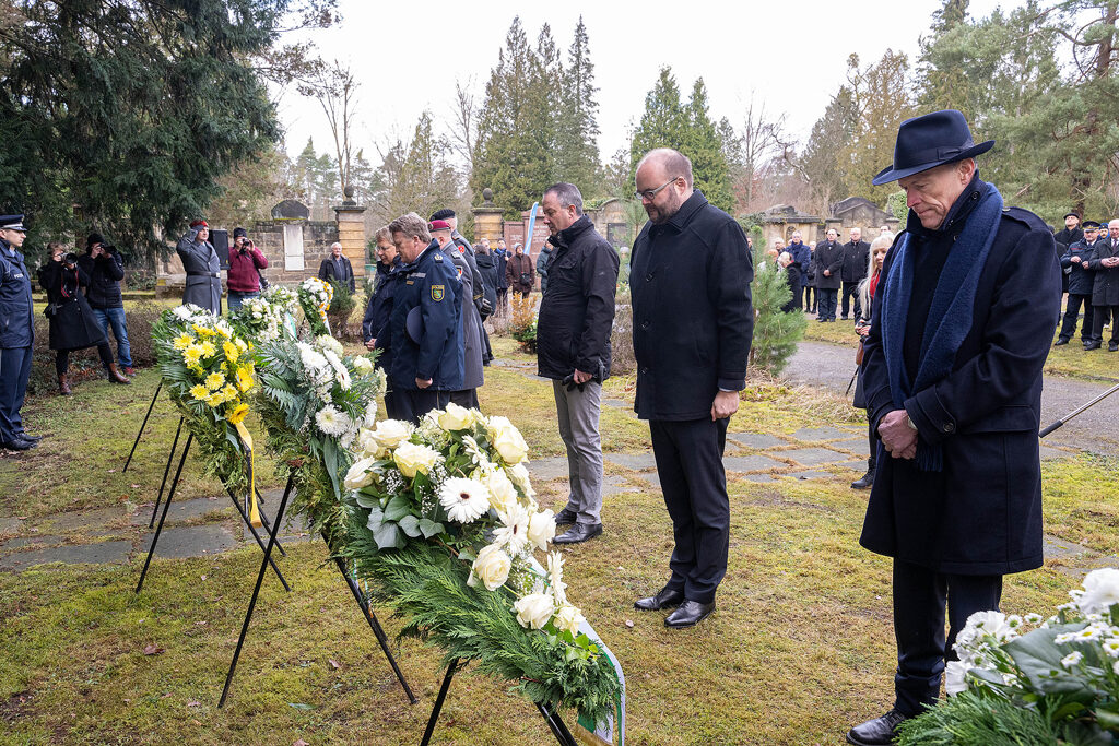 Menschen in stillem Gedenken vor Kränzen auf dem Heidefriedhof