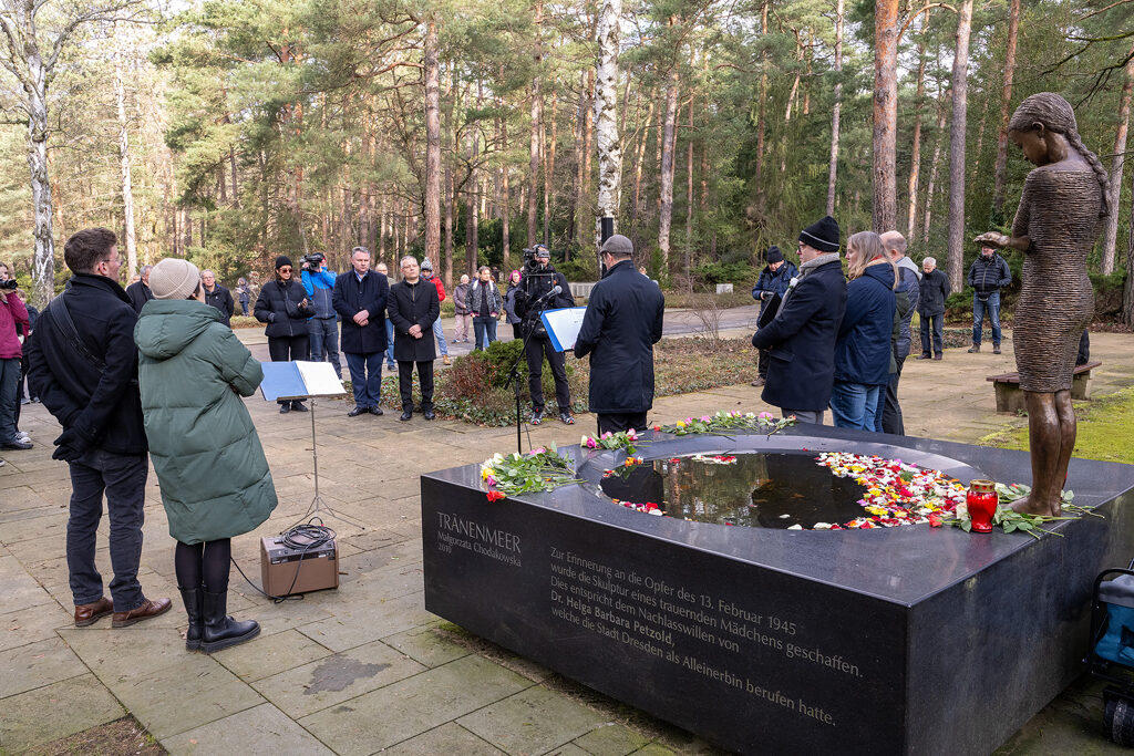 Menschen im Gedenken auf dem Heidefriedhof, im Vordergrund die Skulptur „Trauerndes Mädchen am Tränenmeer“