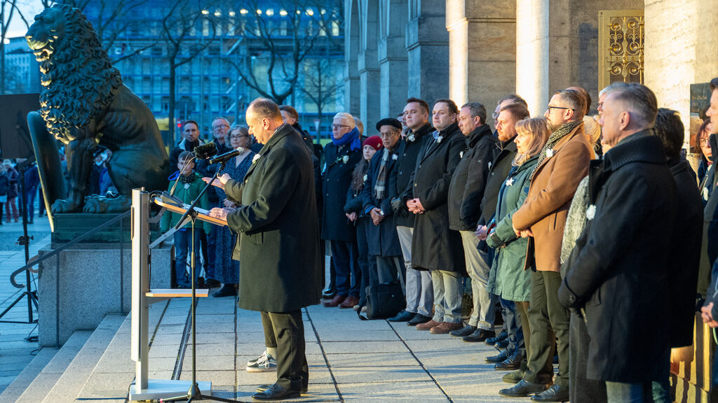 Der Oberbürgermeister hält eine Rede vor der Goldenen Pforte des Neuen Rathauses; hinter ihm stehen Menschen