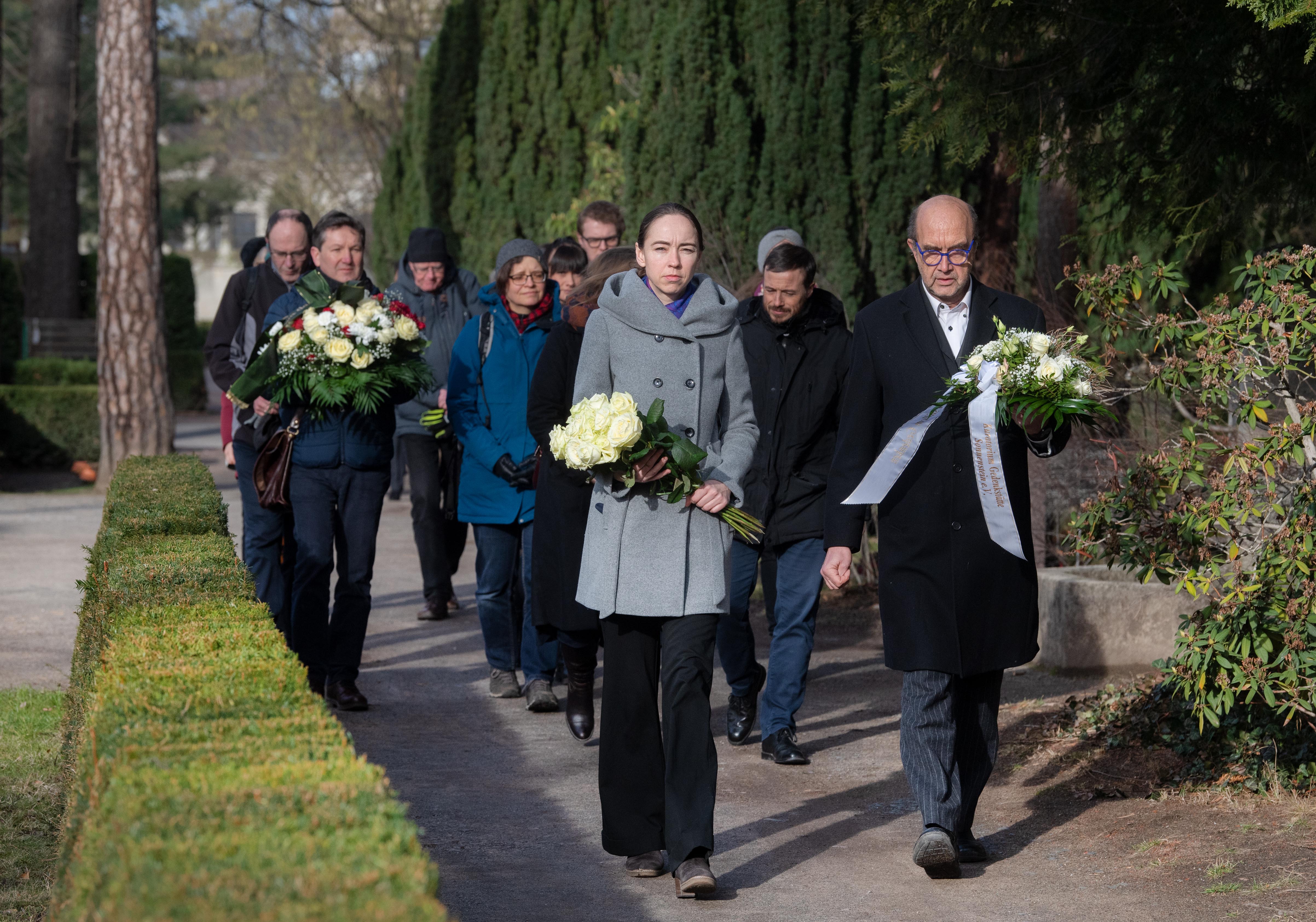 Menschen mit Blumen auf einem Friedhofsweg
