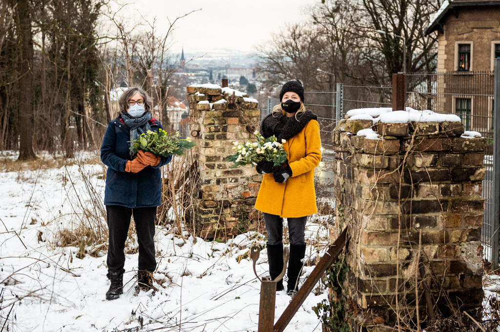 zwei Frauen mit Blumensträußen im Arm vor Mauerpfosten im Schnee