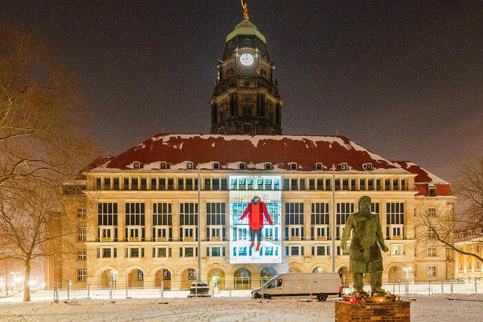 Das Neue Rathaus in Dresden am 13. Februar 2021: An die Fassade ist ein Foto projiziert. Es zeigt eine einzelne Person, die die Hände ausbreitet. Mit diesen Fotos entstand eine virtuelle Menschenkette