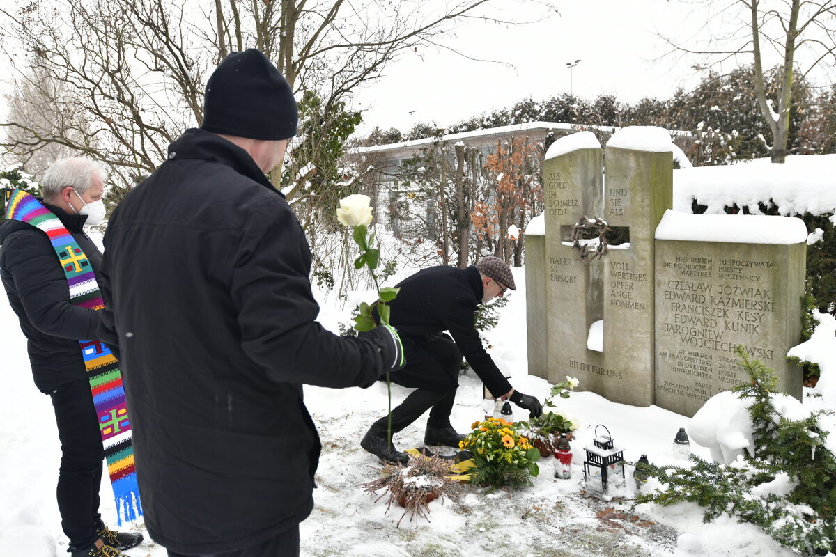 Männer mit weißen Rosen an Gedenksteinen