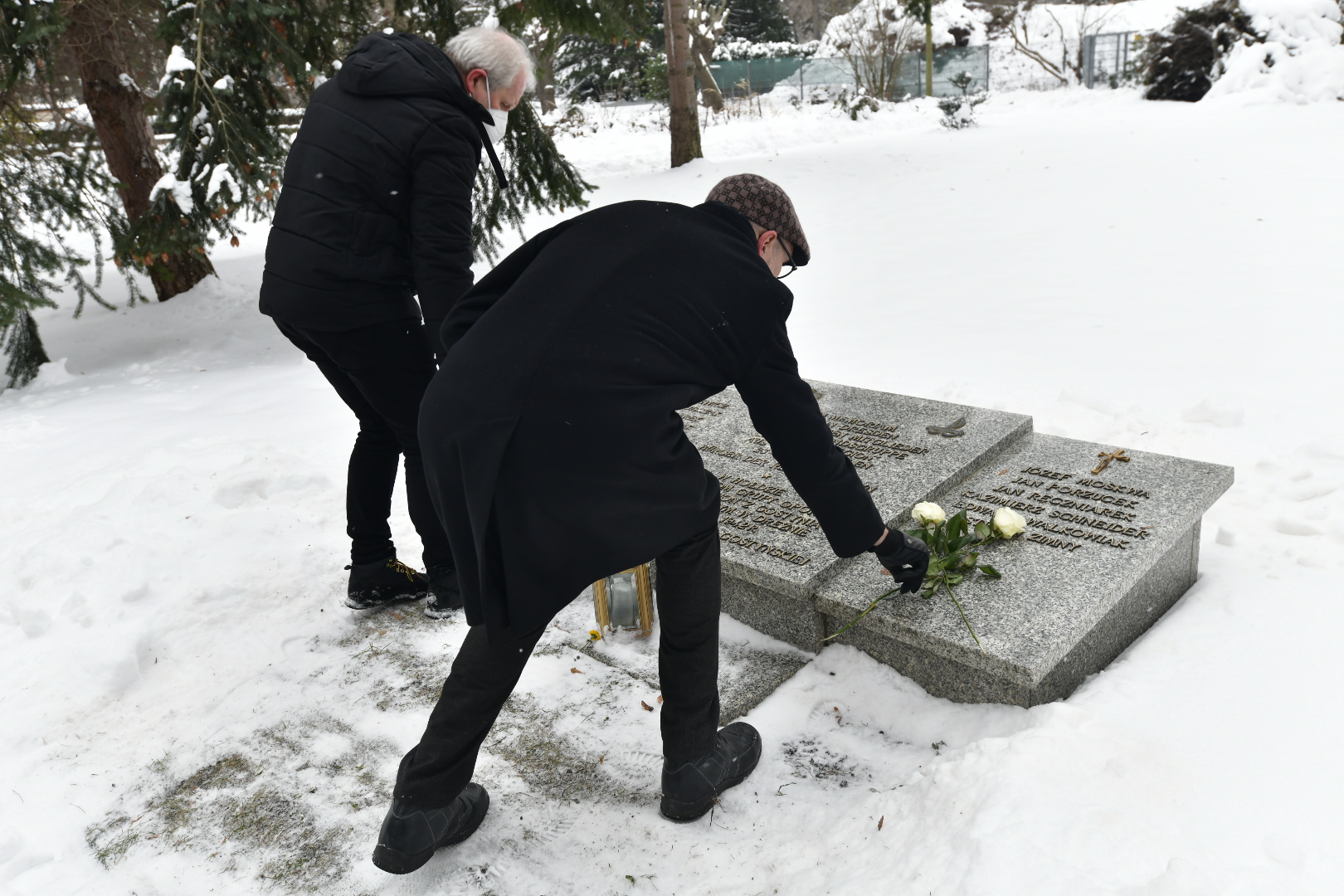 Zwei Männer legen weiße Rosen auf Gedenktafel