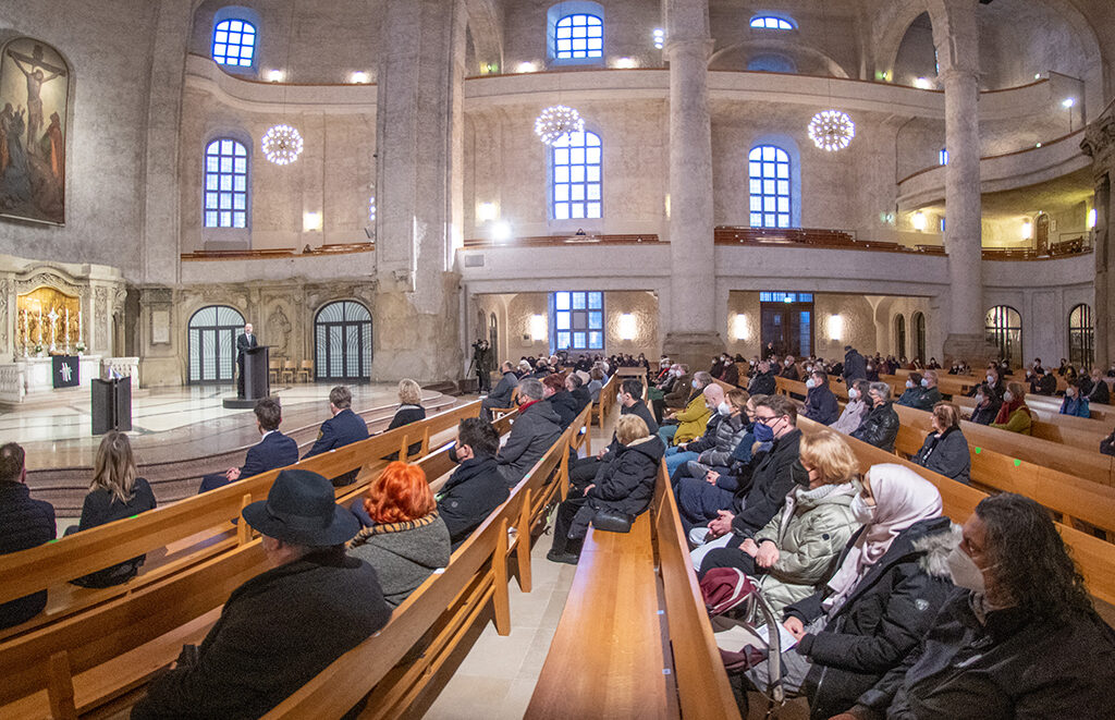 Zuschauer einer Veranstaltung sitzen in den Kirchenbänken in der Kreuzkirche