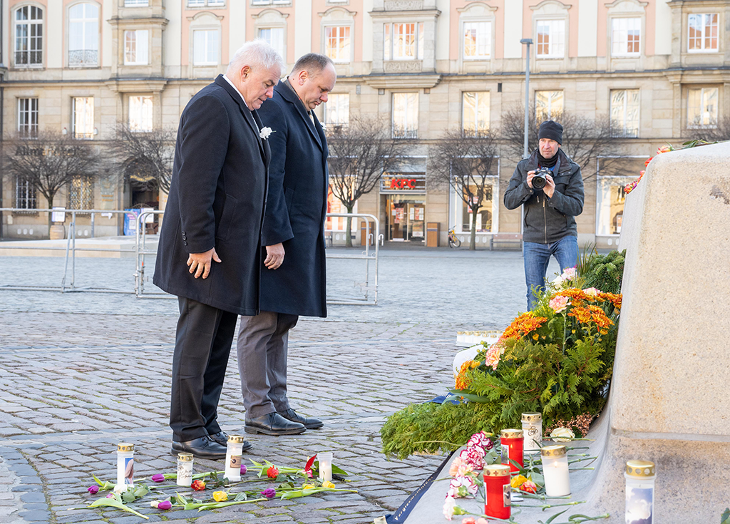 Oberbürgermeister Dirk Hilbert und CDU-Fraktionsvorsitzender Peter Joachim Krüger stehen vor einem Denkmal auf dem Altmarkt in Dresden, darauf stehen Blumenkränze und Kerzen