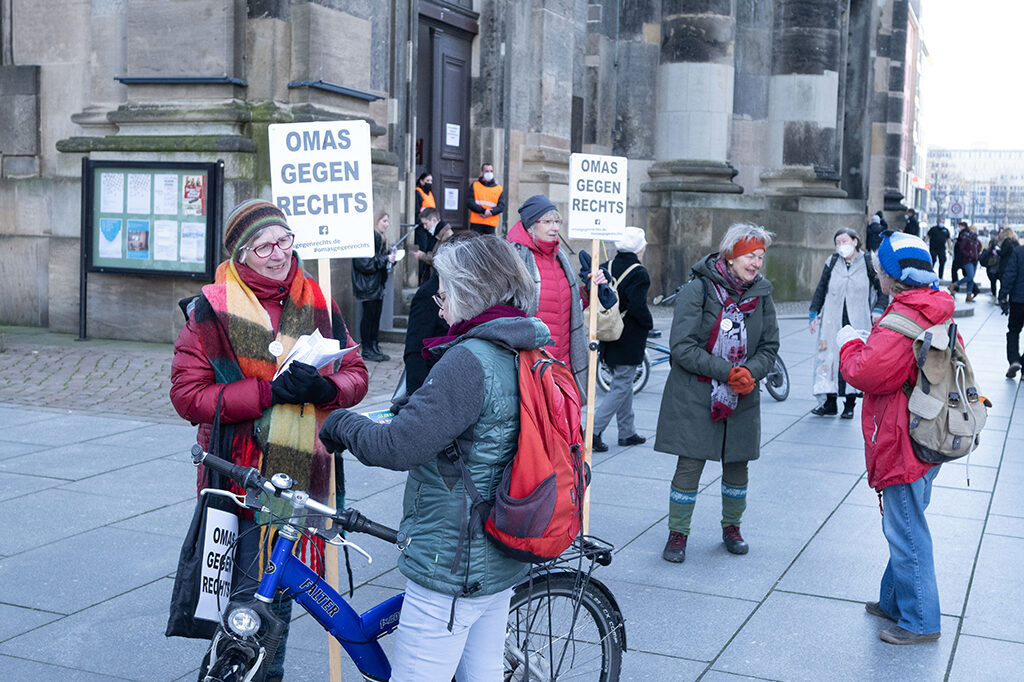 Frauen stehen auf dem Vorplatz der Kreuzkirche zusammen. Sie haben Schilder mit der Aufschrift "Omas gegen Rechts".