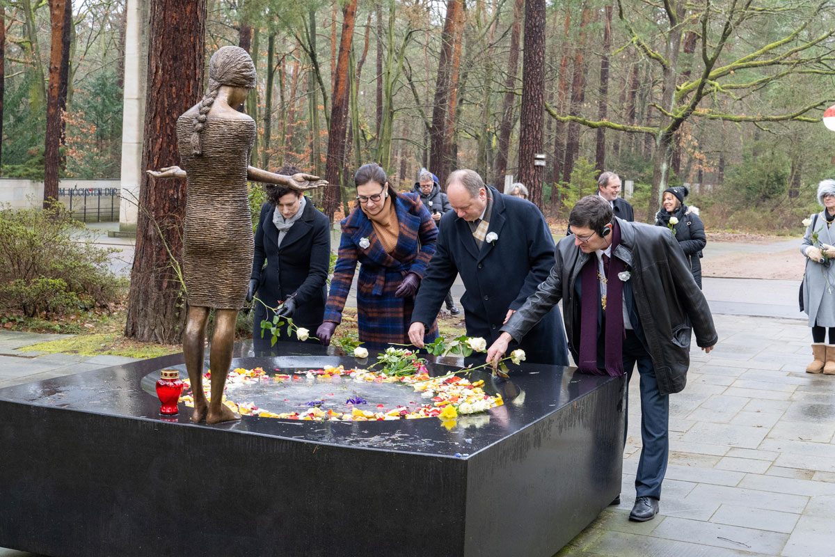Menschen legen Blumen vor einer Bronzefigur nieder