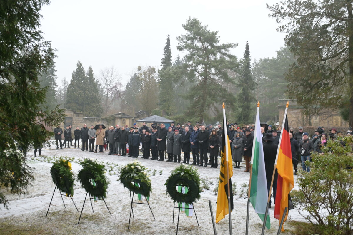 Menschen in stillem Gedenken vor Kränzen auf dem Heidefriedhof