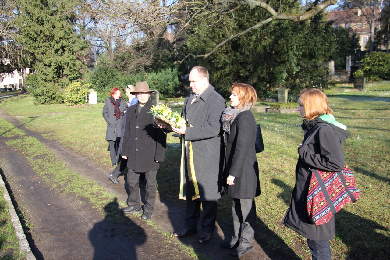 Menschen stehen auf dem Friedhof, Oberbürgermeister Dirk Hilbert hält ein Blumengesteck