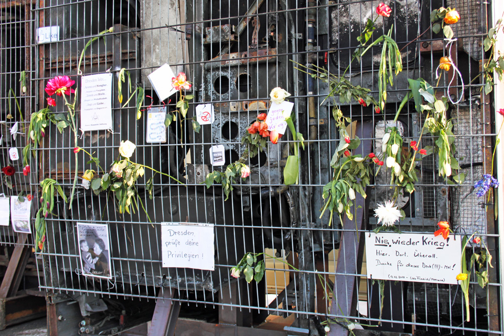 Blumen und Zettel am Gitter vor der Skulptur Monument